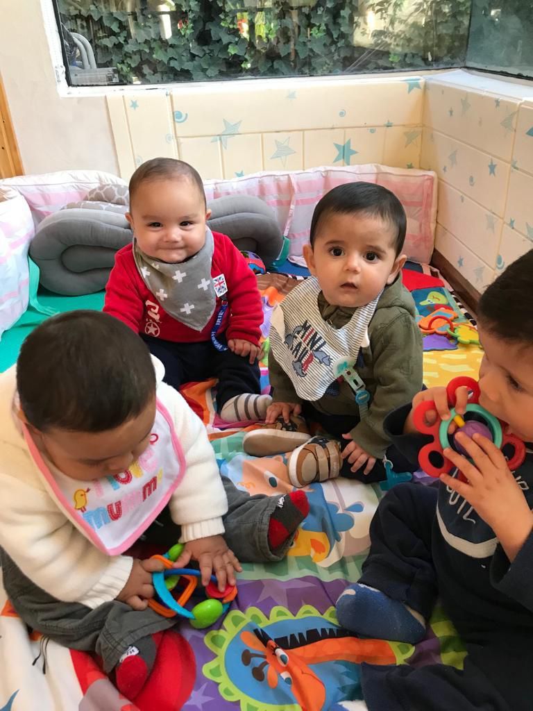 El área infantil: cuatro niños pequeños jugando juntos entre cojines y juguetes.
