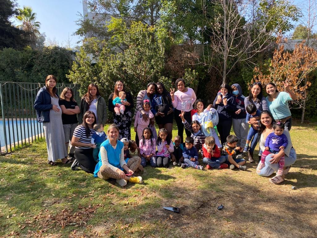 Un encuentro al aire libre: mamás, hijos y voluntarias reunidos bajo los árboles.