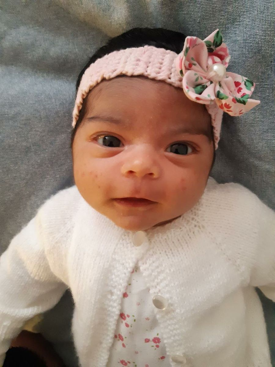 Una guagua recién nacida, despierta, con una cinta con flores en el pelo.