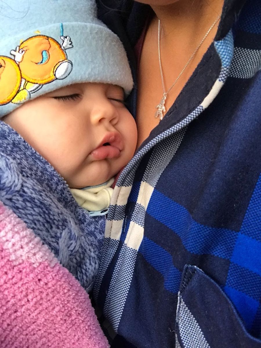 Una mamá abrigando a su guagua dormida contra el pecho.