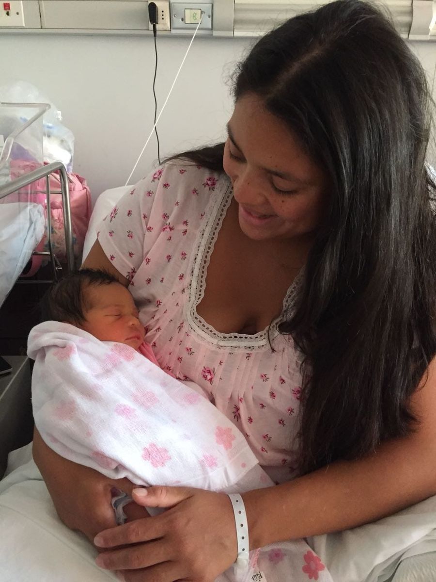 Una mamá sonriendo con su hija recién nacida en brazos.