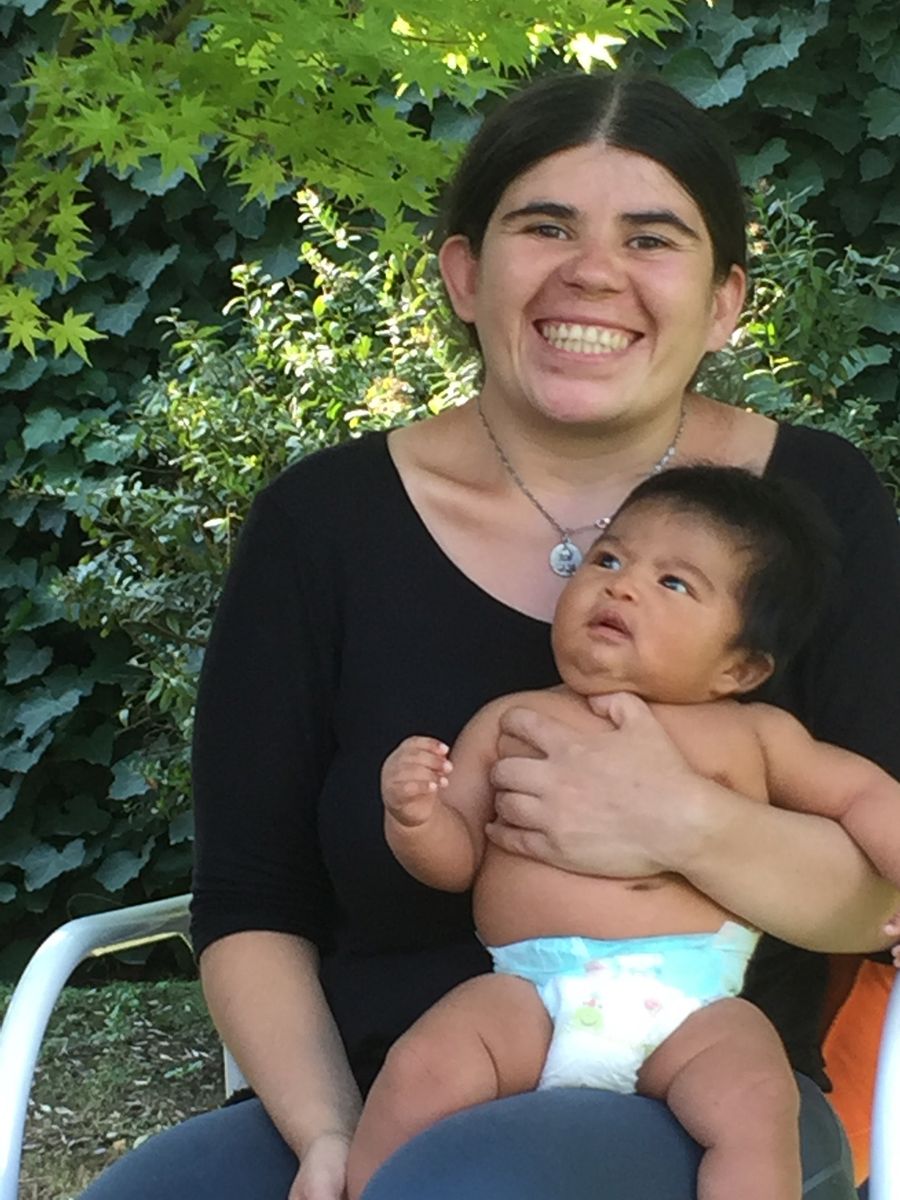 Una mamá sonriendo en el jardín de la casa, con su guagua sentada en la falda.